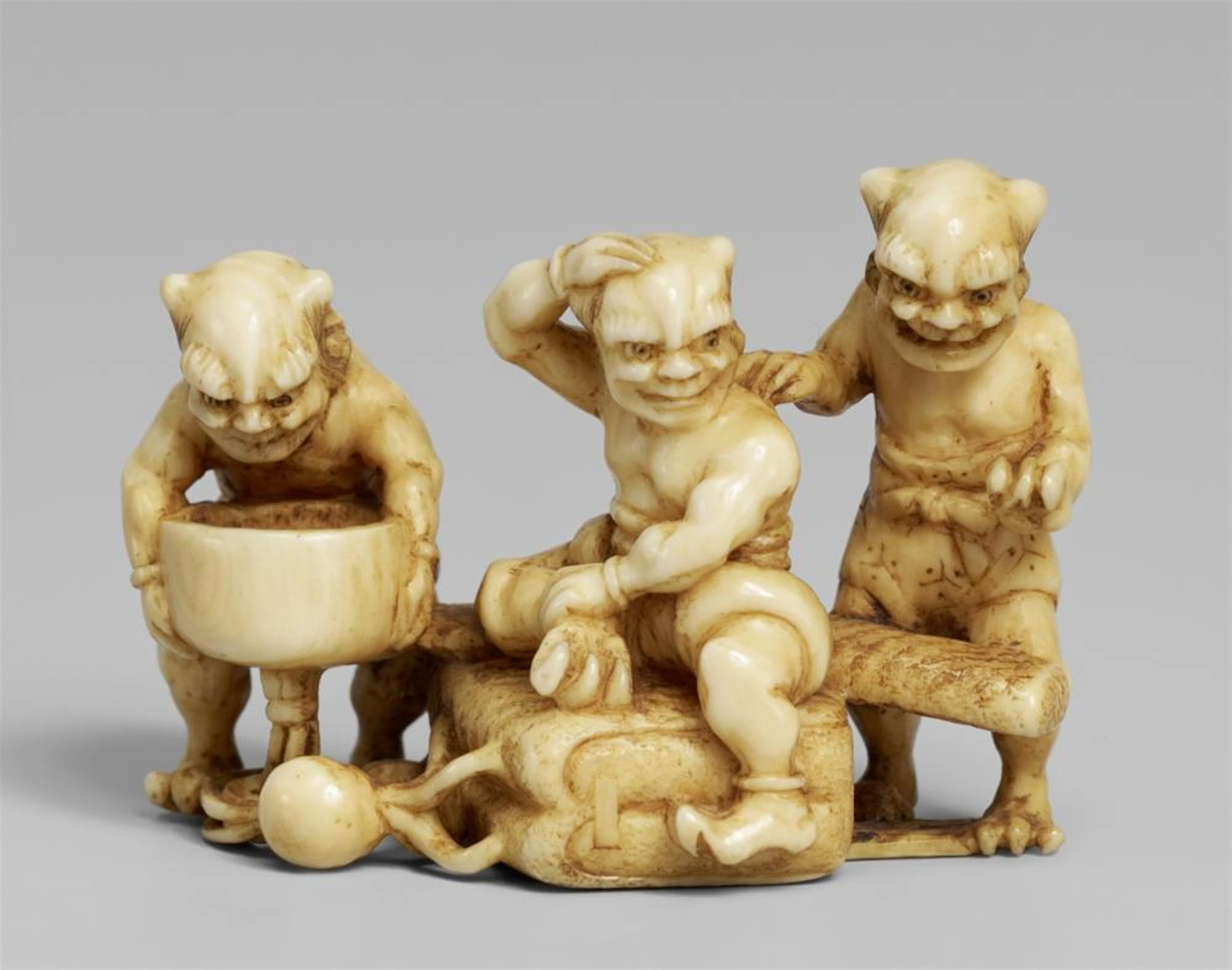 An ivory netsuke of three oni with a smoking set. Late 19th century