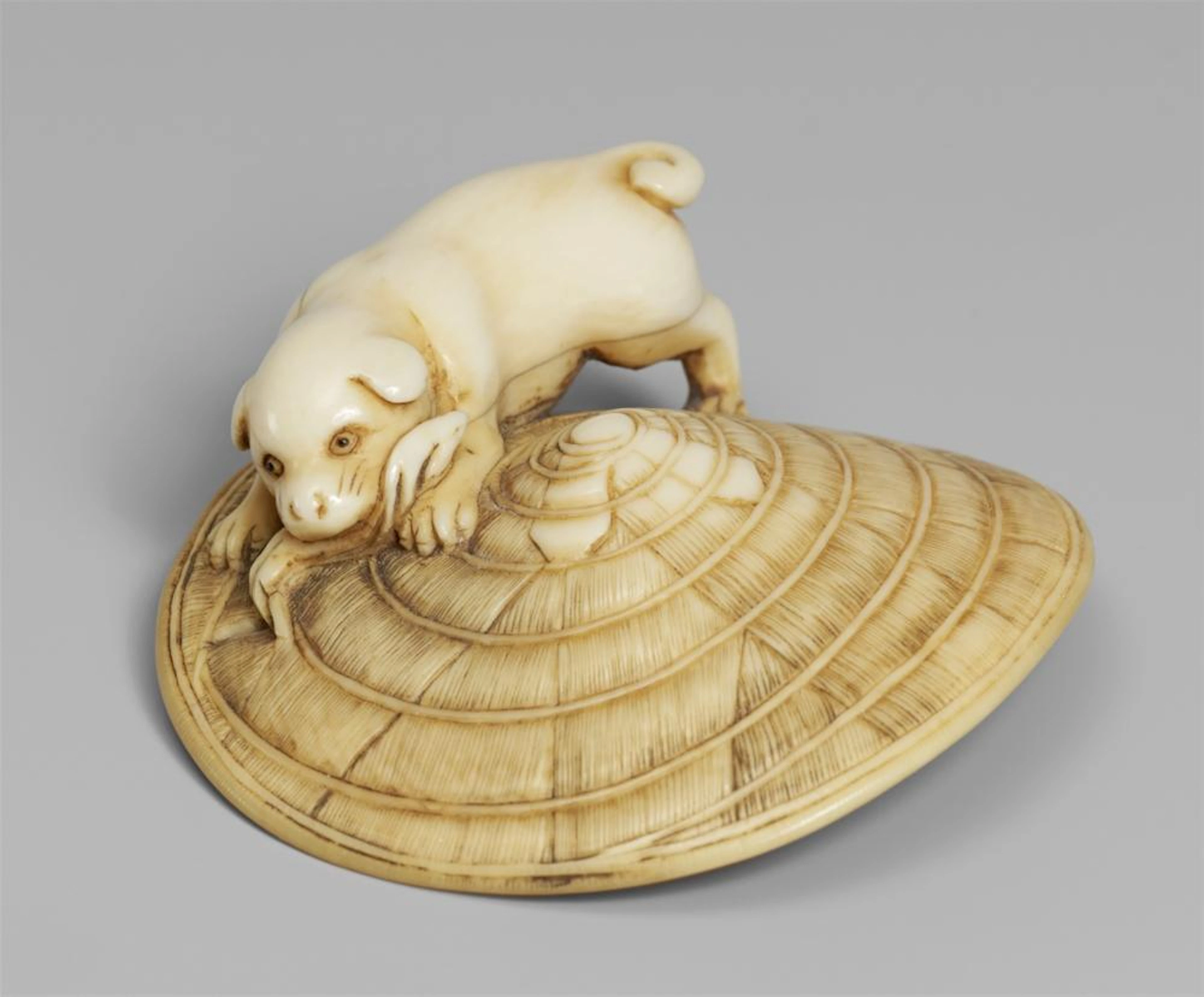 An ivory netsuke of a dog on a straw hat. Mid-19th century