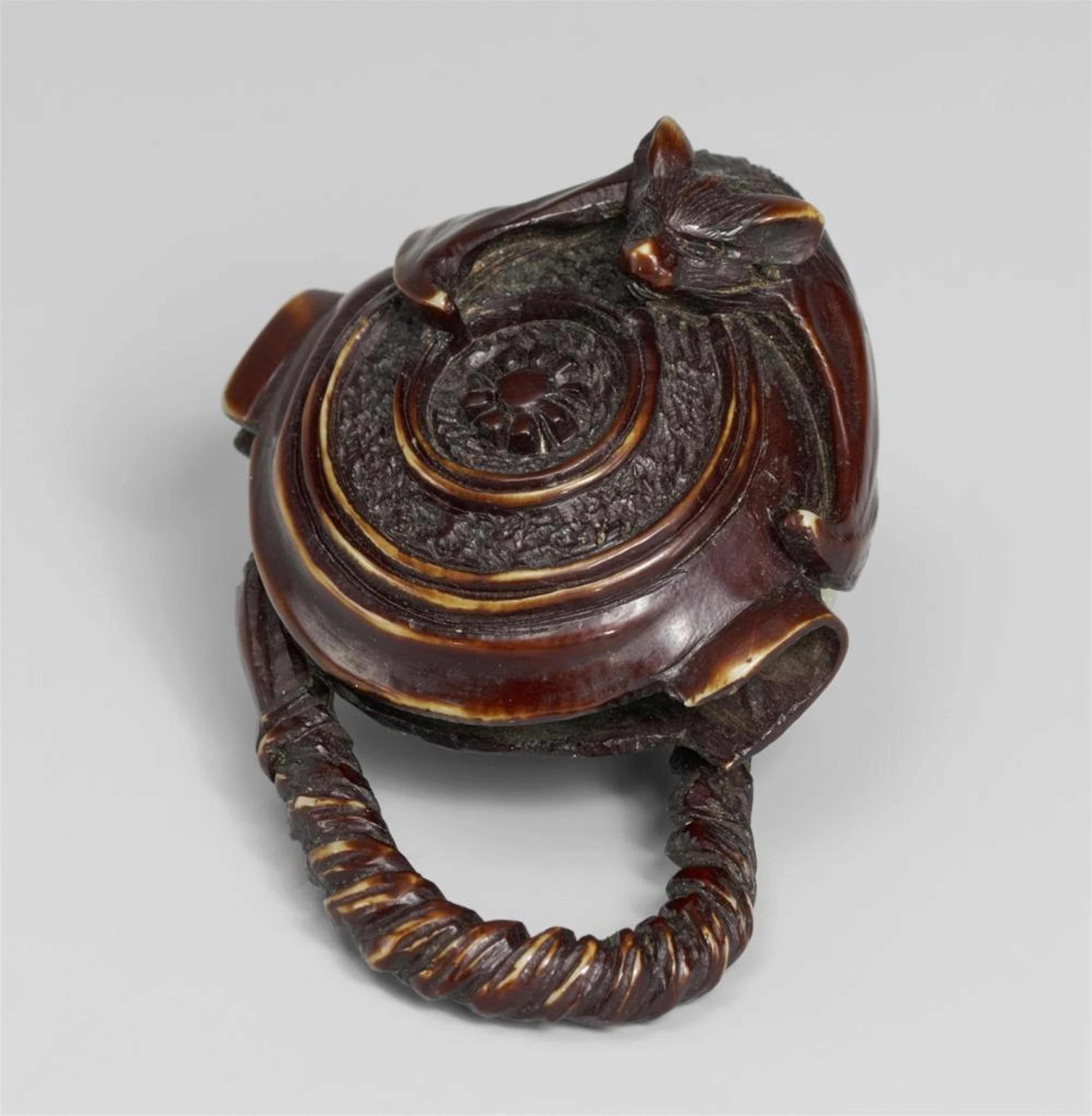 A stained ivory netsuke of a bat on a Buddhist gong. Osaka. Late 19th century