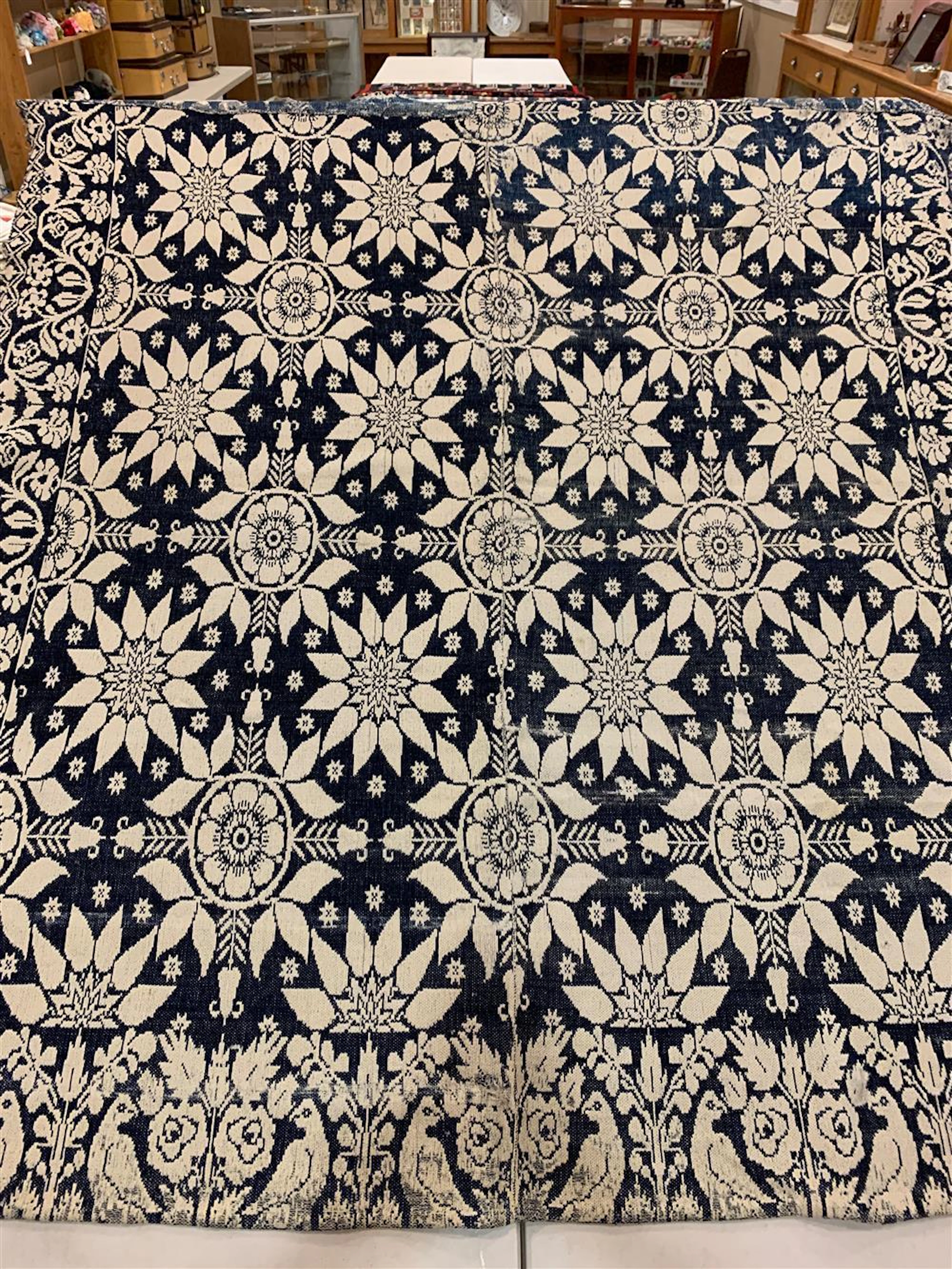 70" X 73" VINTAGE NAVY AND ECRU FLORAL COVERLET. MARTIN HAMANN WOVEN IN. SOME REPAIRS NEEDED AND SOME REPAIRS MADE. STAINED.