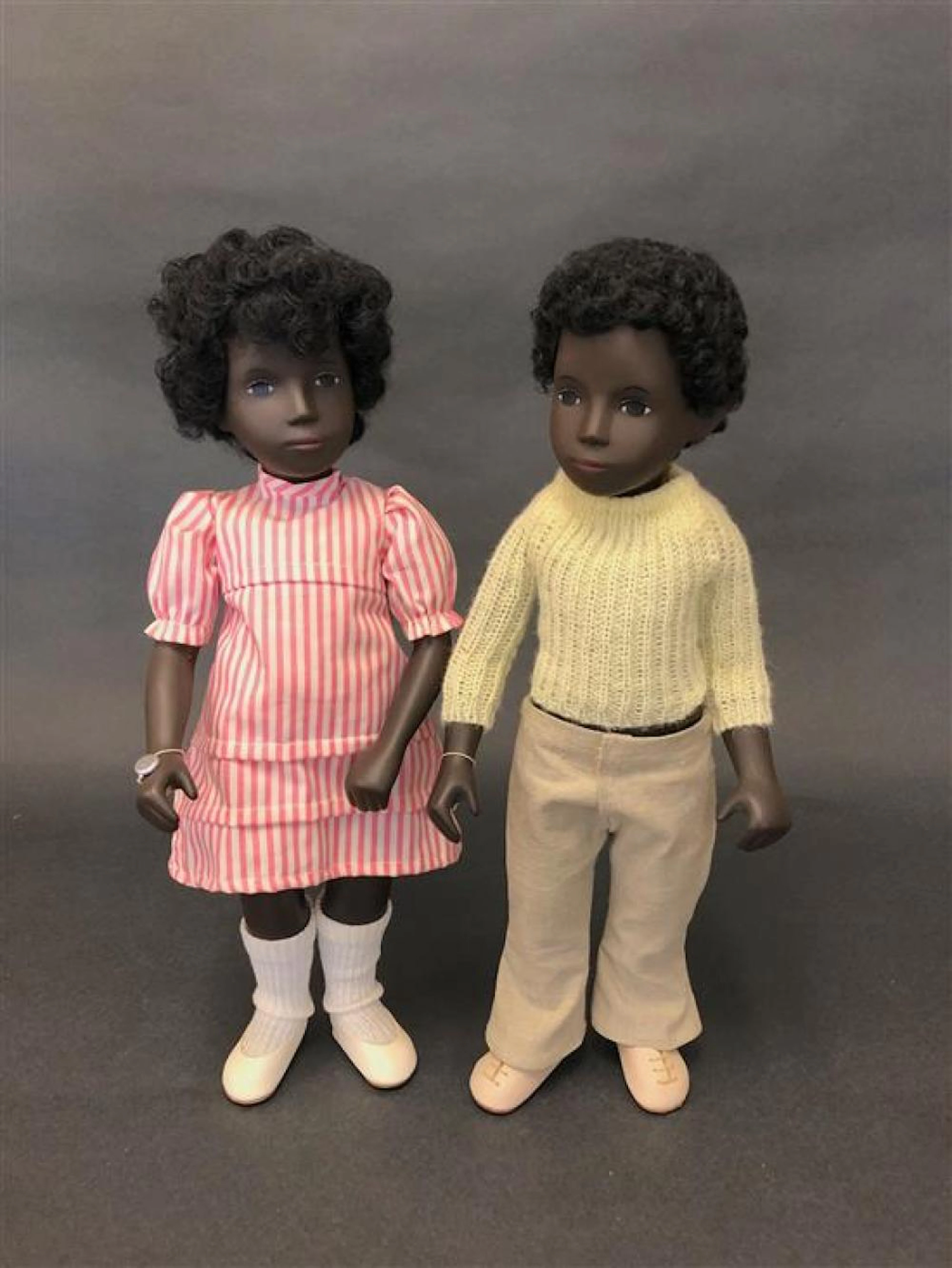 (2) 16½" VINTAGE BLACK SASHA TRENDON ENGLAND DOLLS - CORA SUMMER DRESS AND CALEB SWEATER #318. BOTH WEAR RED CIRCLE DOT SERIE WRIST...