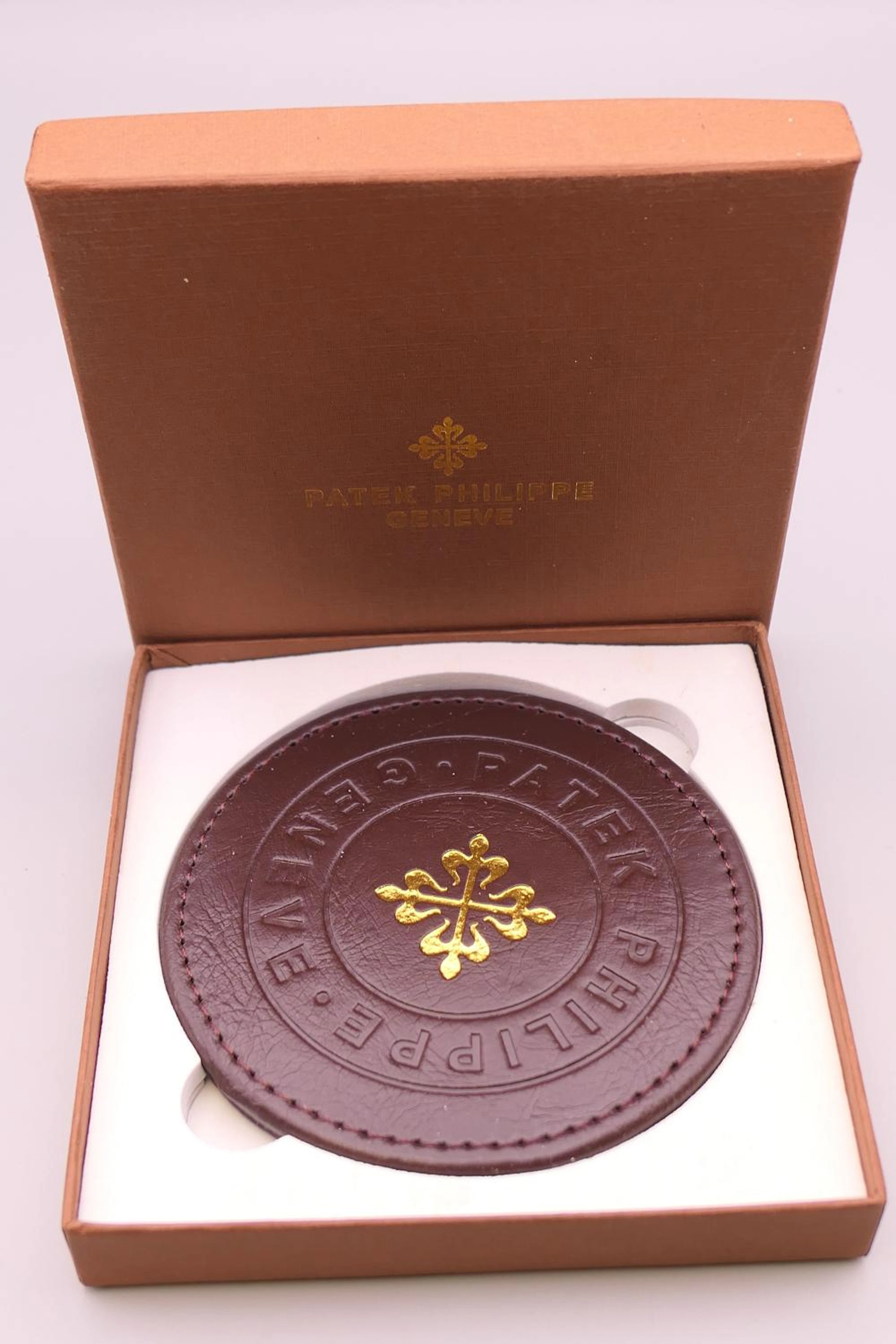 A Patek Philipp Geneve coaster, boxed. 10 cm diameter.