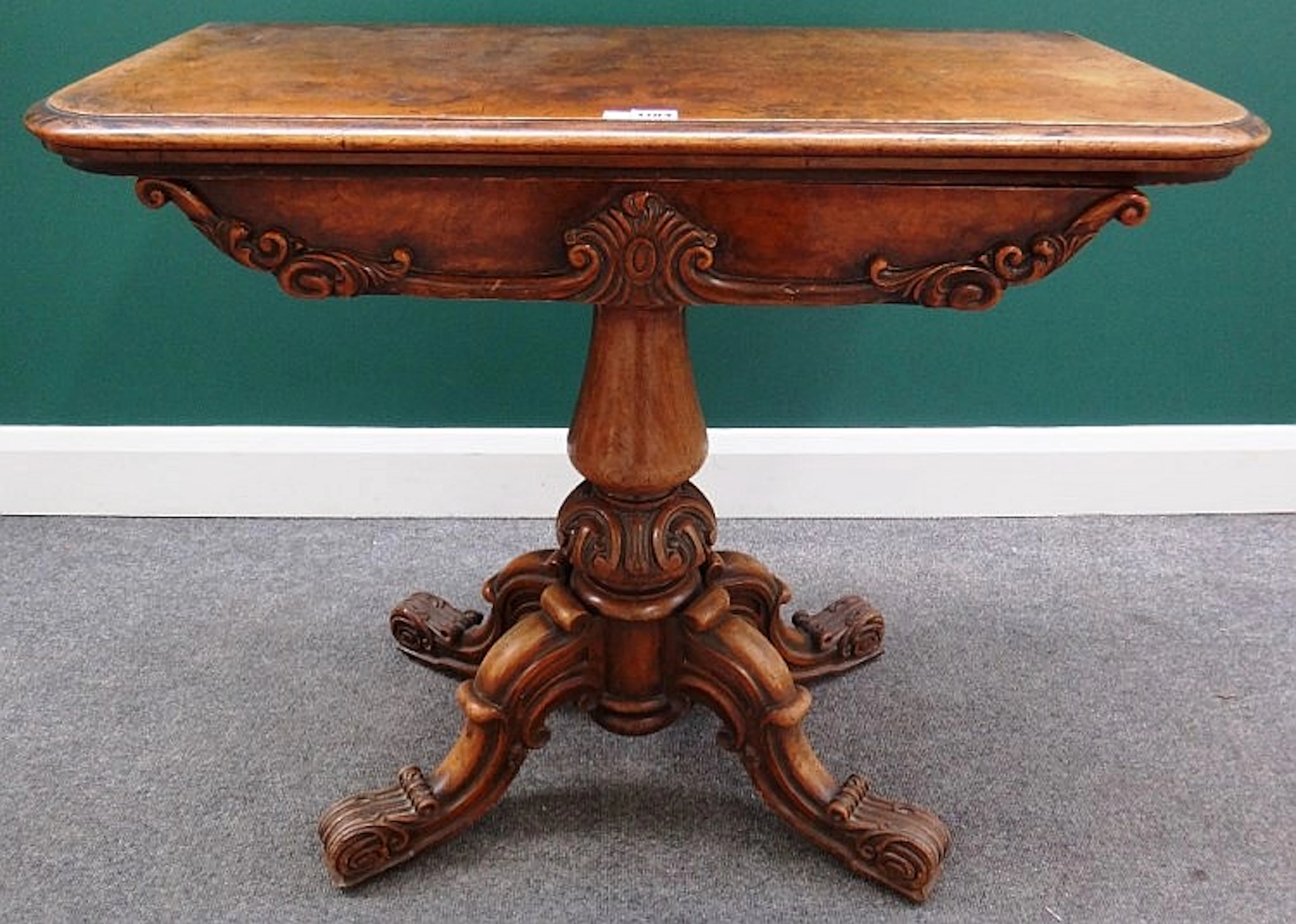 A Victorian figured walnut card table with carved frieze, on turned column