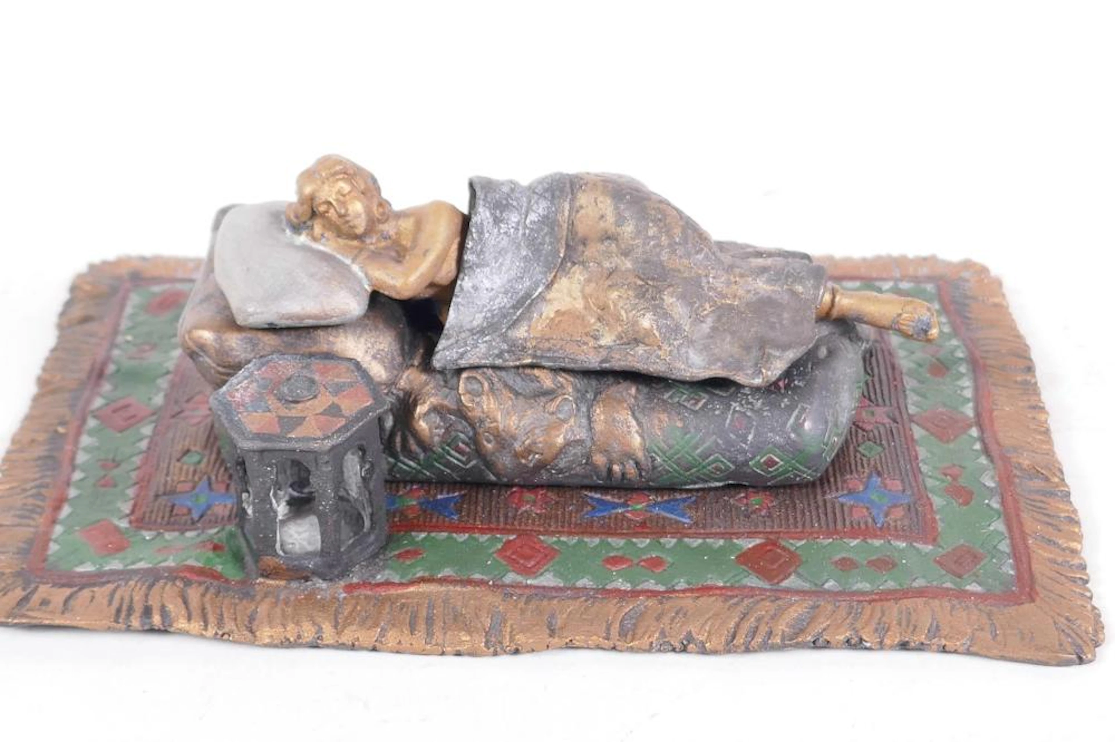 A cold painted bronze figure of a woman lying on a couch set on a Persian rug