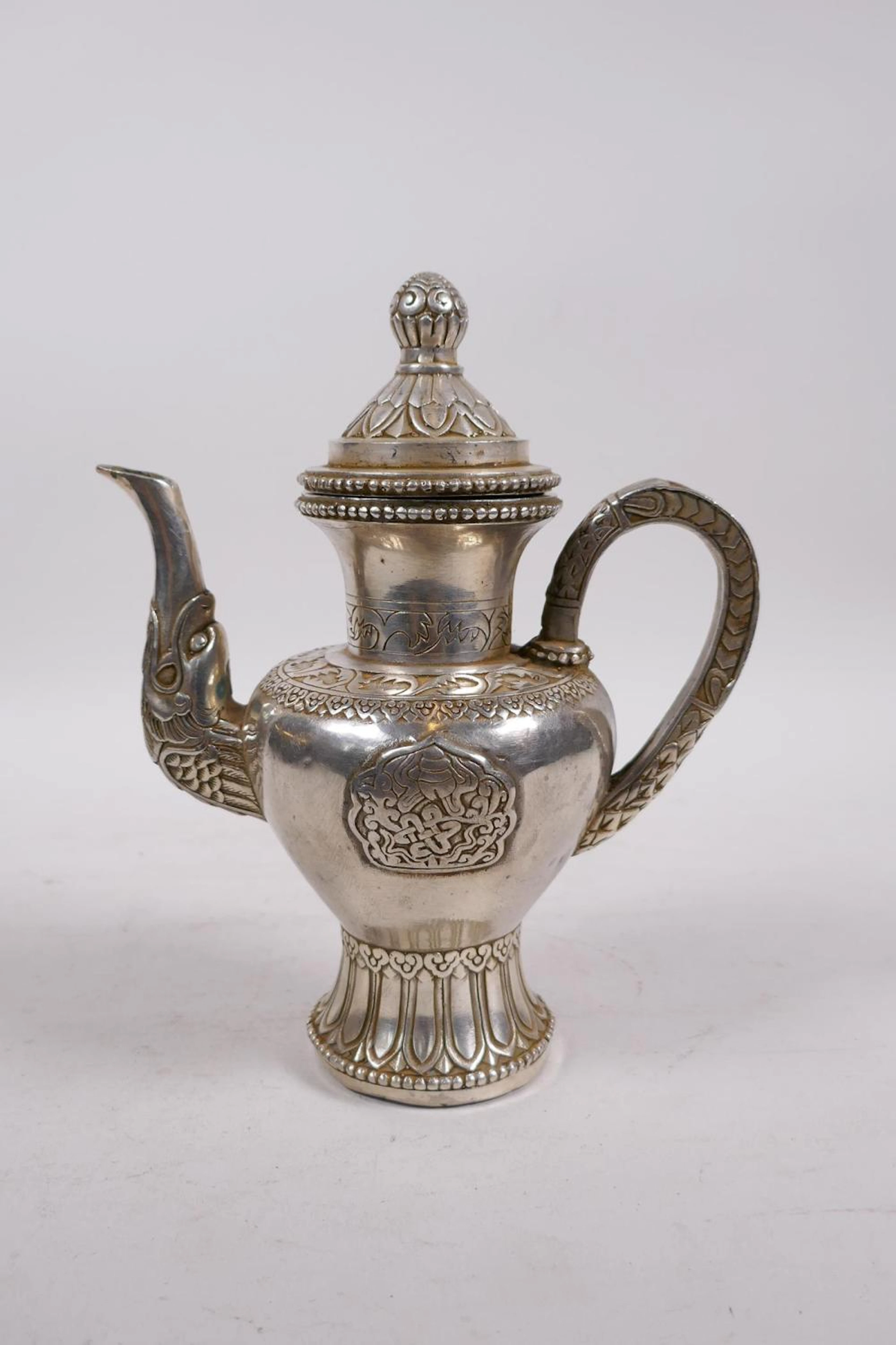 A Tibetan white metal teapot decorated with Buddhist emblems