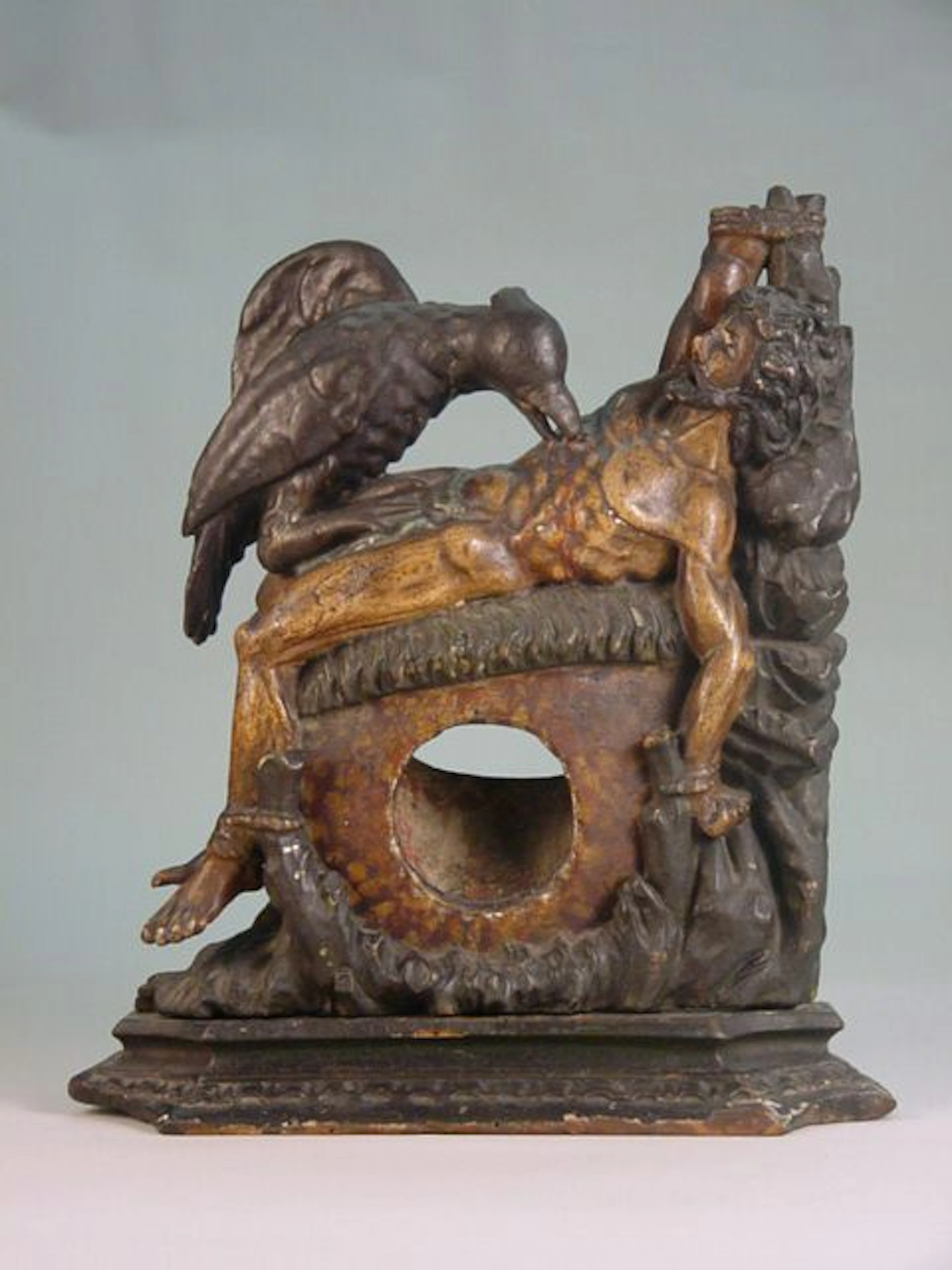 German, 18th century.Carved and polychrome painted wood watch holder, representing a large, black bird attacking a dying man, tied to a tree by his hands and feet